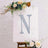Decorative floral letter "N" on an easel with greenery and flowers.
