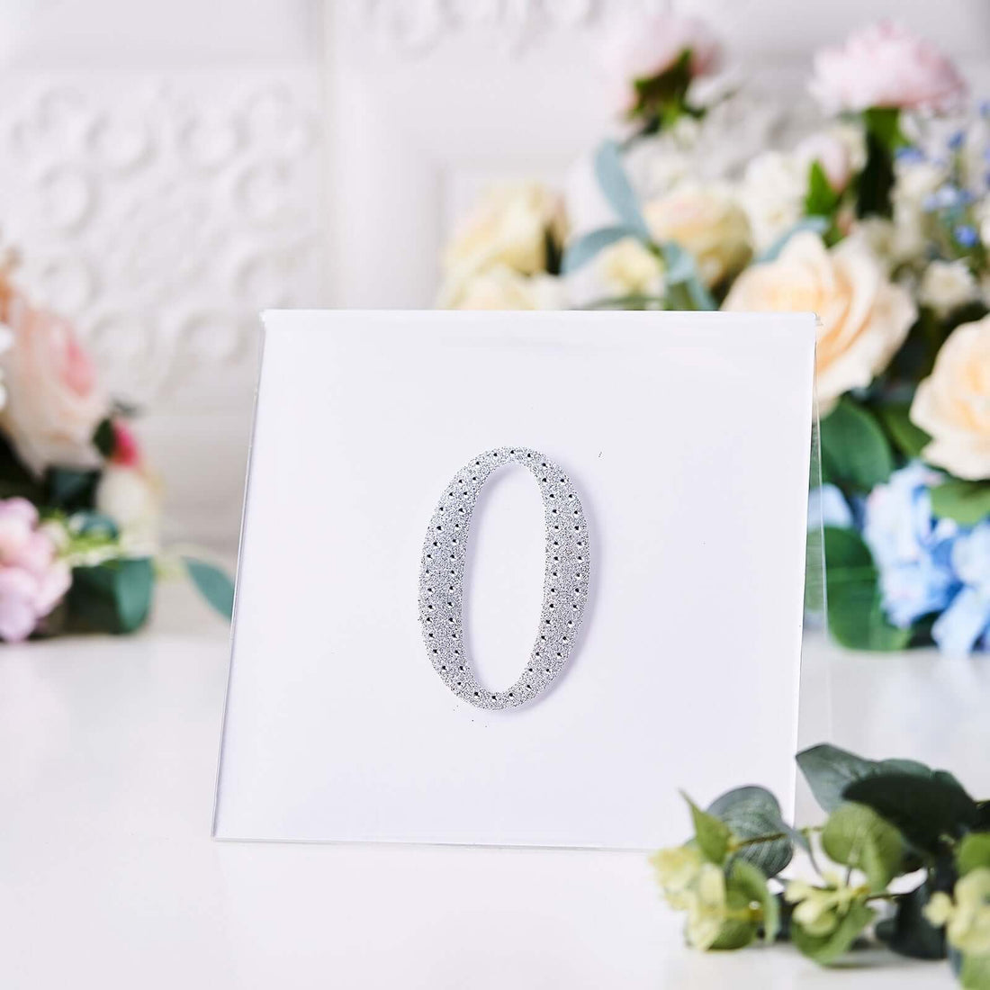 Silver decorative number "0" on a plain white backdrop.