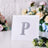 Glittery silver letter "P" on a white card surrounded by flowers.