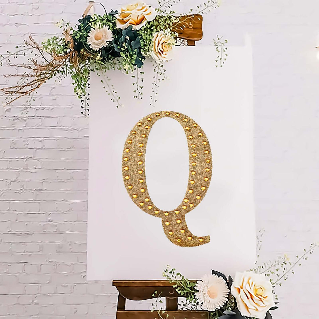 Gold rhinestone letter Q on a white poster with floral decorations.
