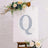 Glittery letter Q on a canvas with floral accents and a wooden easel.