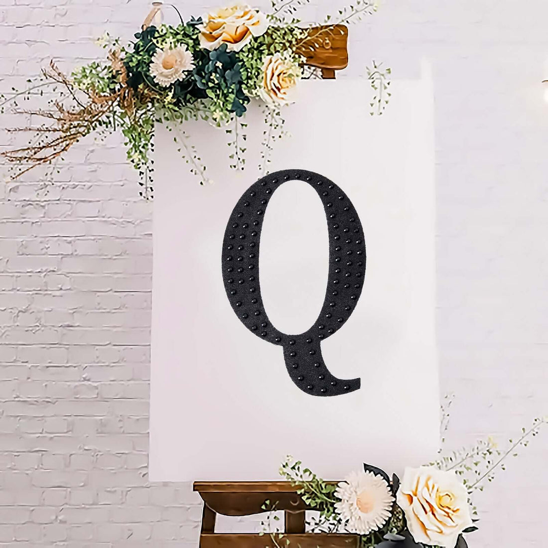 Decorative letter "Q" art on canvas with floral accents.
