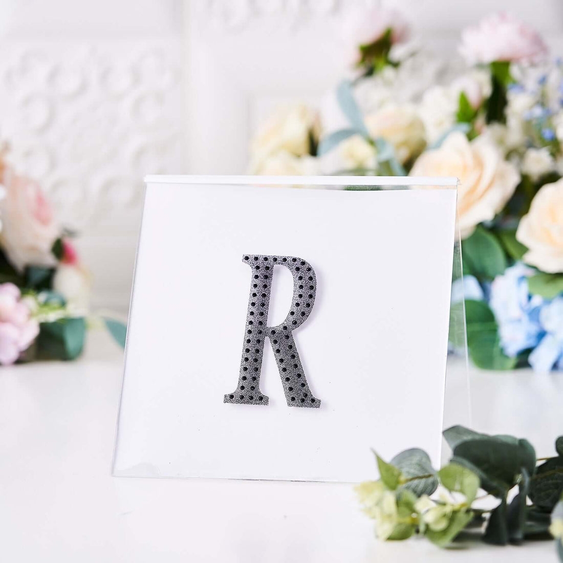 Decorative letter "R" in black rhinestones on a clear display stand.