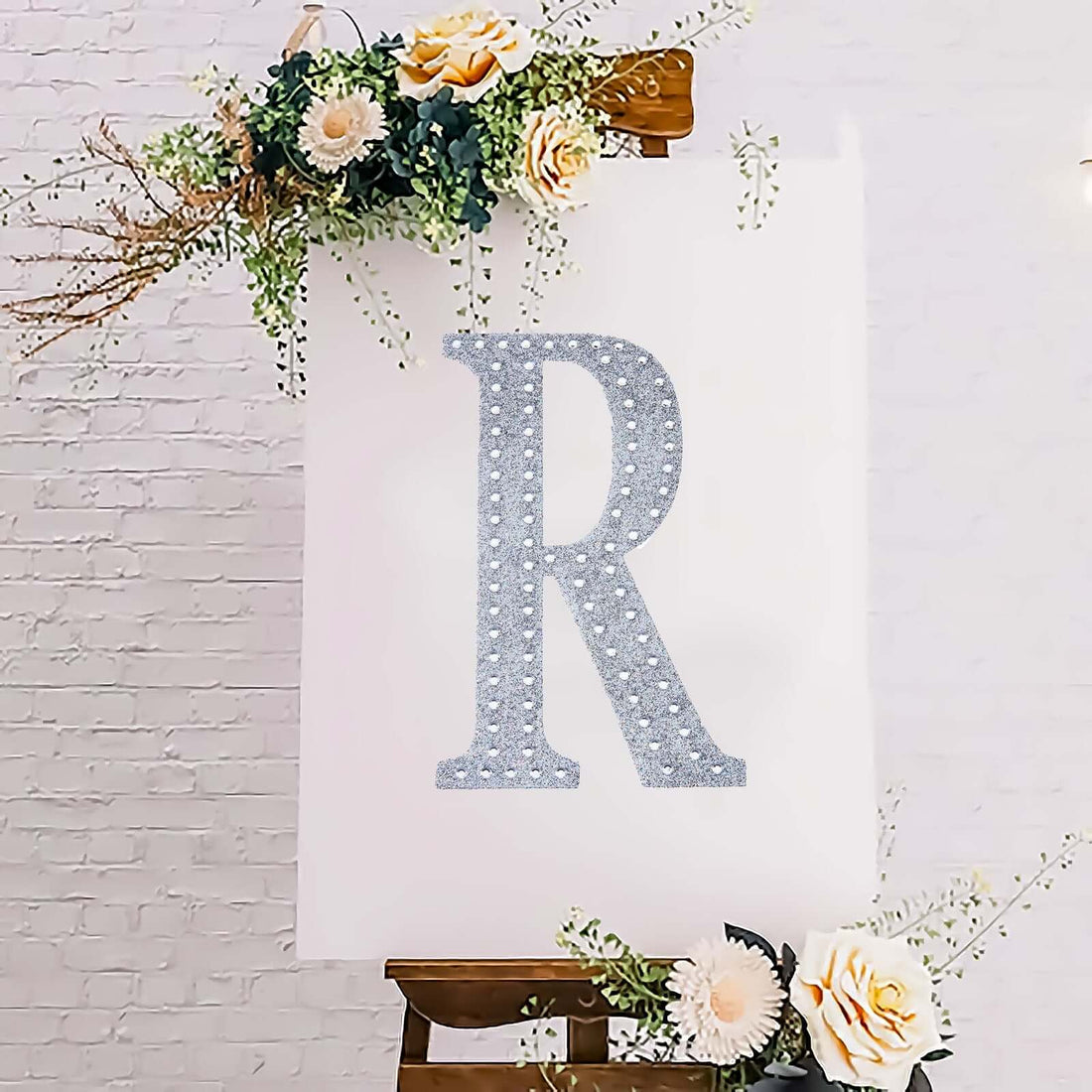 Decorative glitter letter "R" on a floral backdrop.