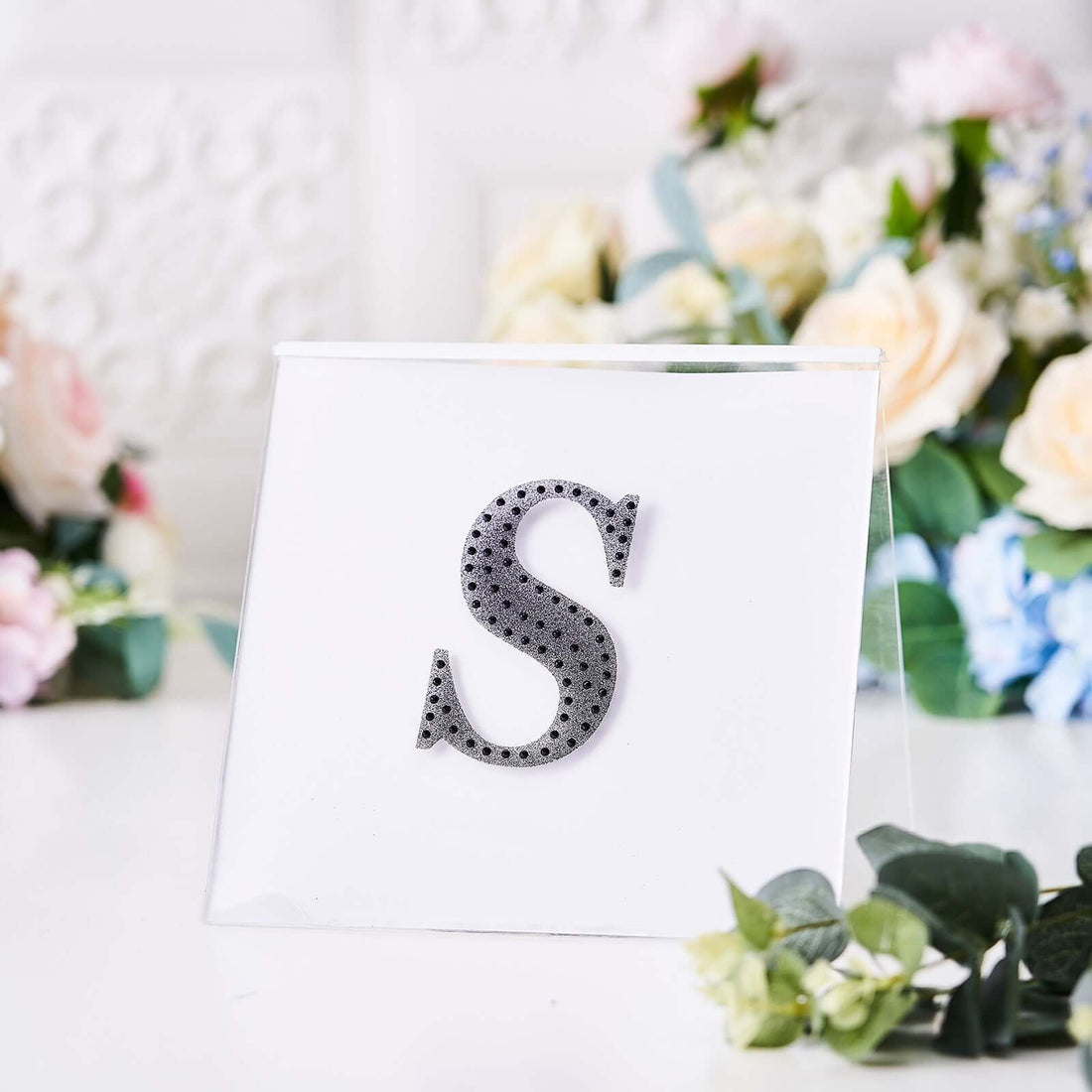 Decorative letter "S" in rhinestones displayed on a clear acrylic stand.