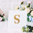 Gold rhinestone letter "S" decorative piece on a white base.