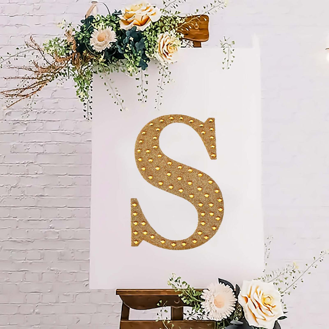 Gold glitter letter "S" on a decorative canvas with flowers