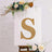 Gold glitter letter "S" on a decorative canvas with flowers