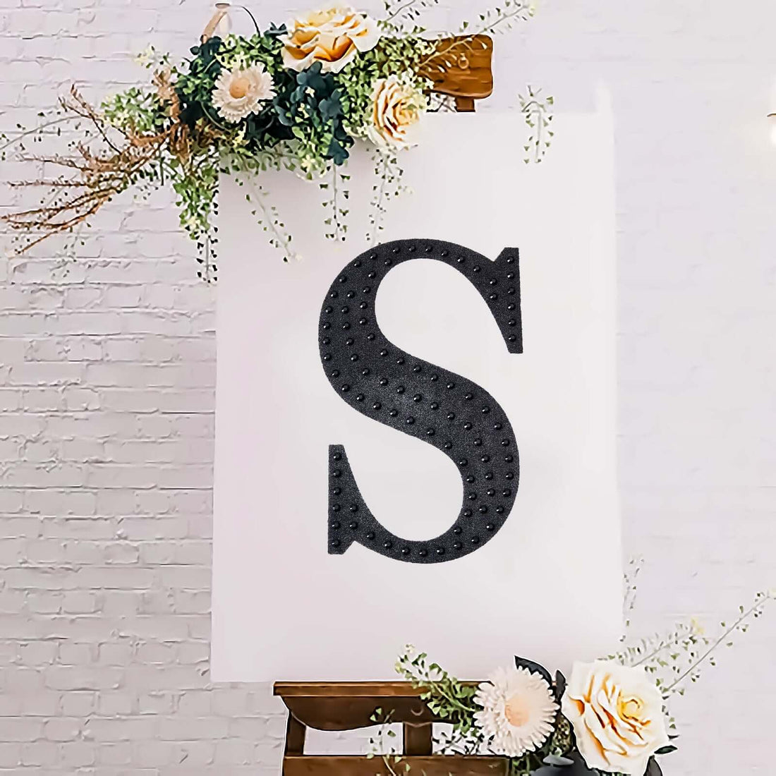 Decorative black letter "S" on an easel with floral accents.