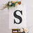 Decorative black letter "S" on an easel with floral accents.