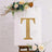 Gold glitter letter "T" on a decorative easel with floral accents.
