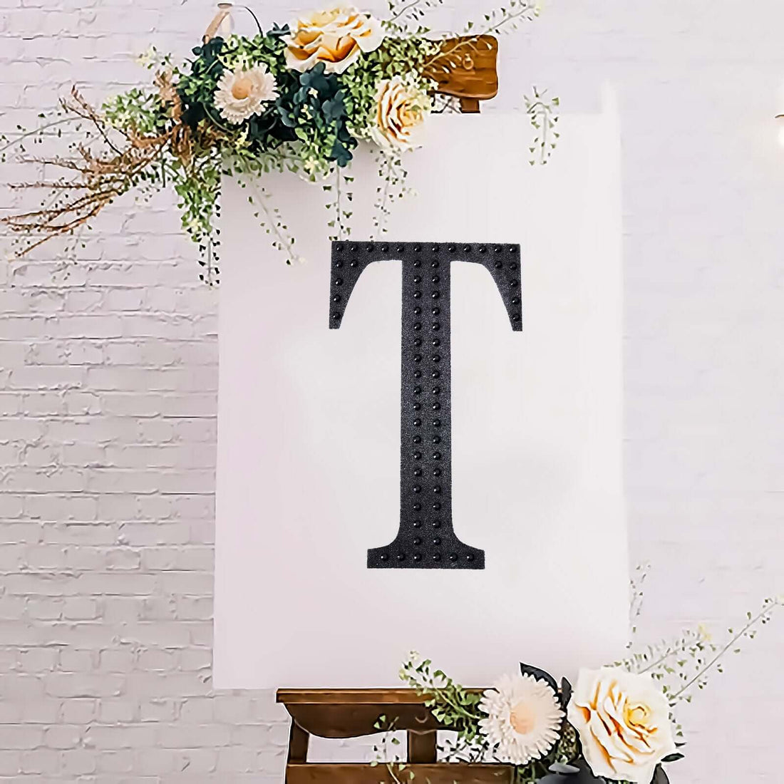 Decorative letter 'T' on an easel with floral accents.