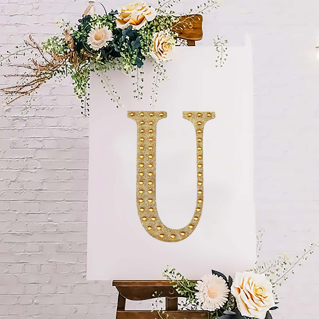 Decorative letter "U" with lights on an easel surrounded by flowers.