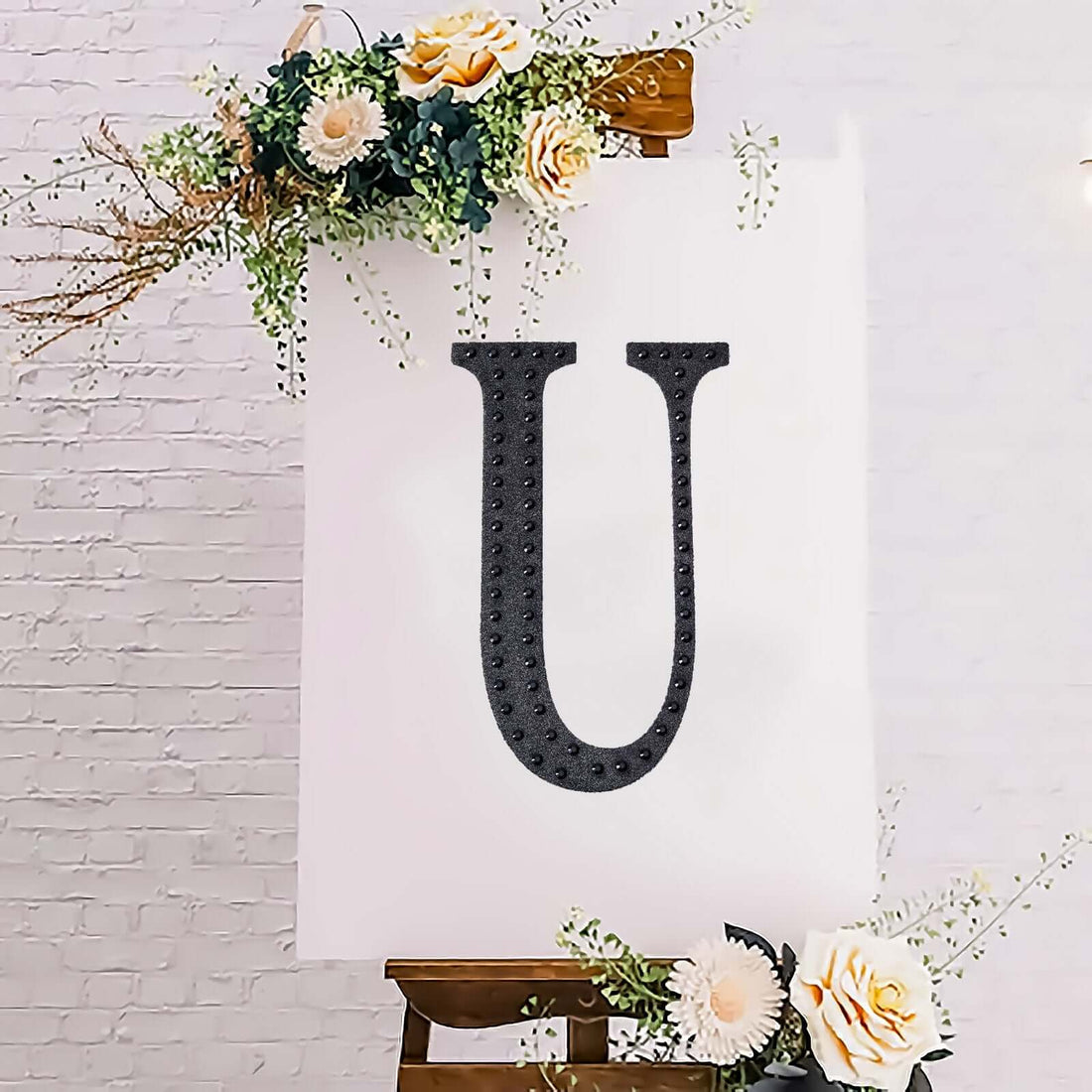 Black marquee letter "U" on a backdrop with flowers.