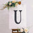 Black marquee letter "U" on a backdrop with flowers.