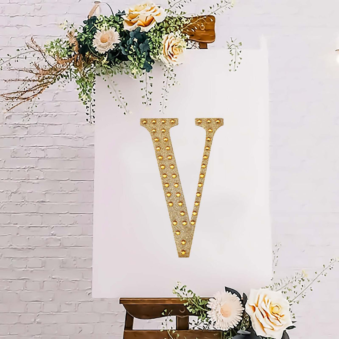 Gold studded letter V on a canvas with floral accents.