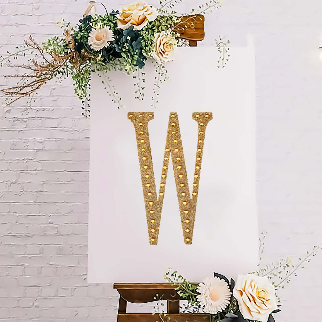 Gold marquee letter "W" on an easel with floral accents.