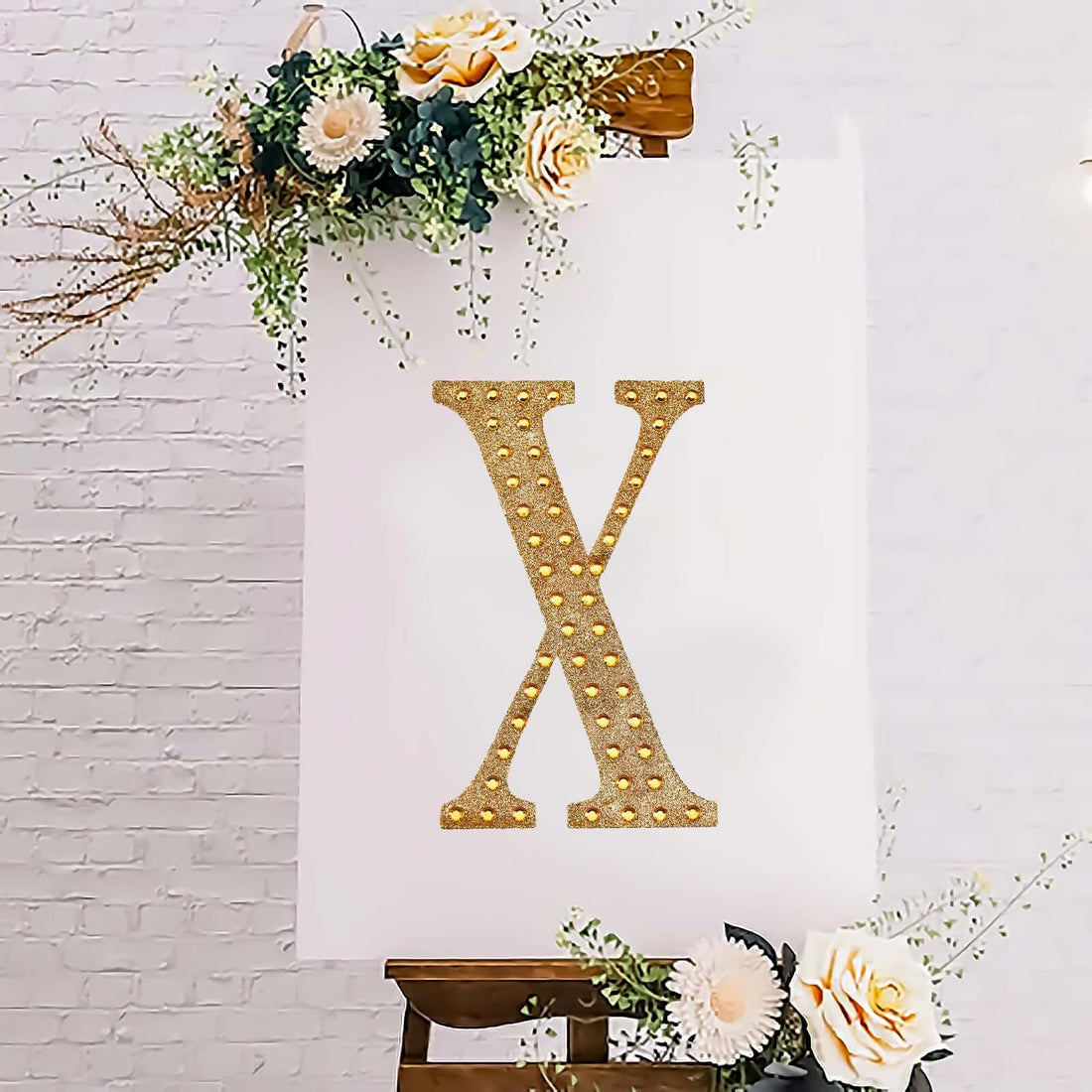 Gold marquee letter X on an easel with floral decorations.
