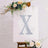 Decorative letter "X" on a floral backdrop with an easel.