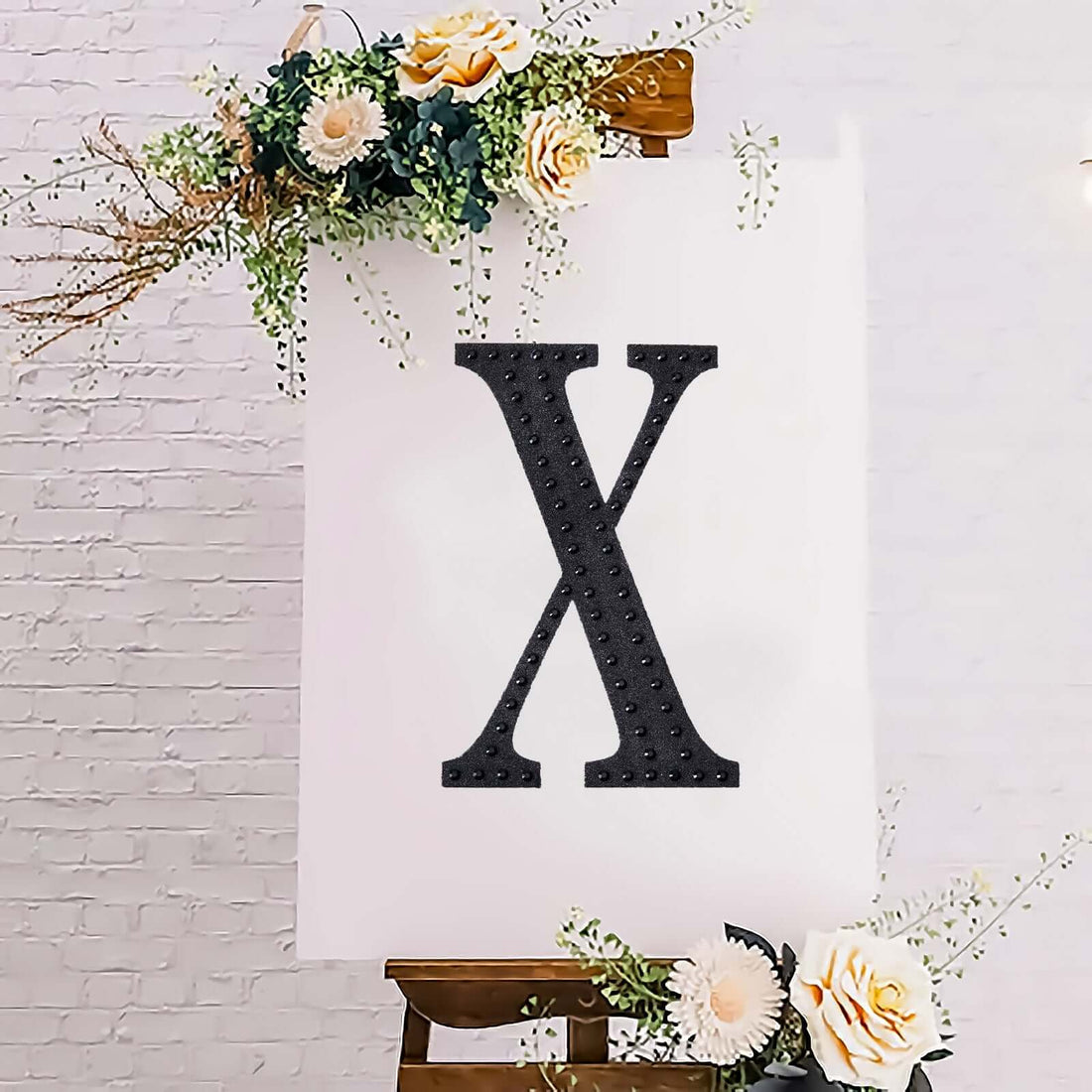 Black decorative letter "X" on an easel with floral accents.