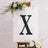 Black decorative letter "X" on an easel with floral accents.