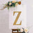 Decorative gold letter "Z" with lights on an easel surrounded by flowers.