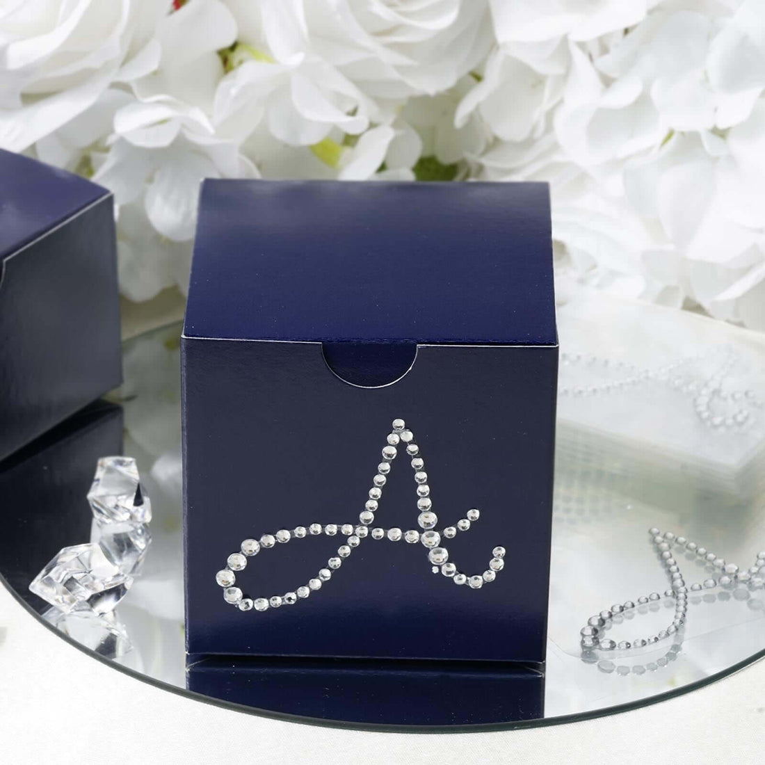 Navy gift box adorned with rhinestone letter "A" against floral backdrop.