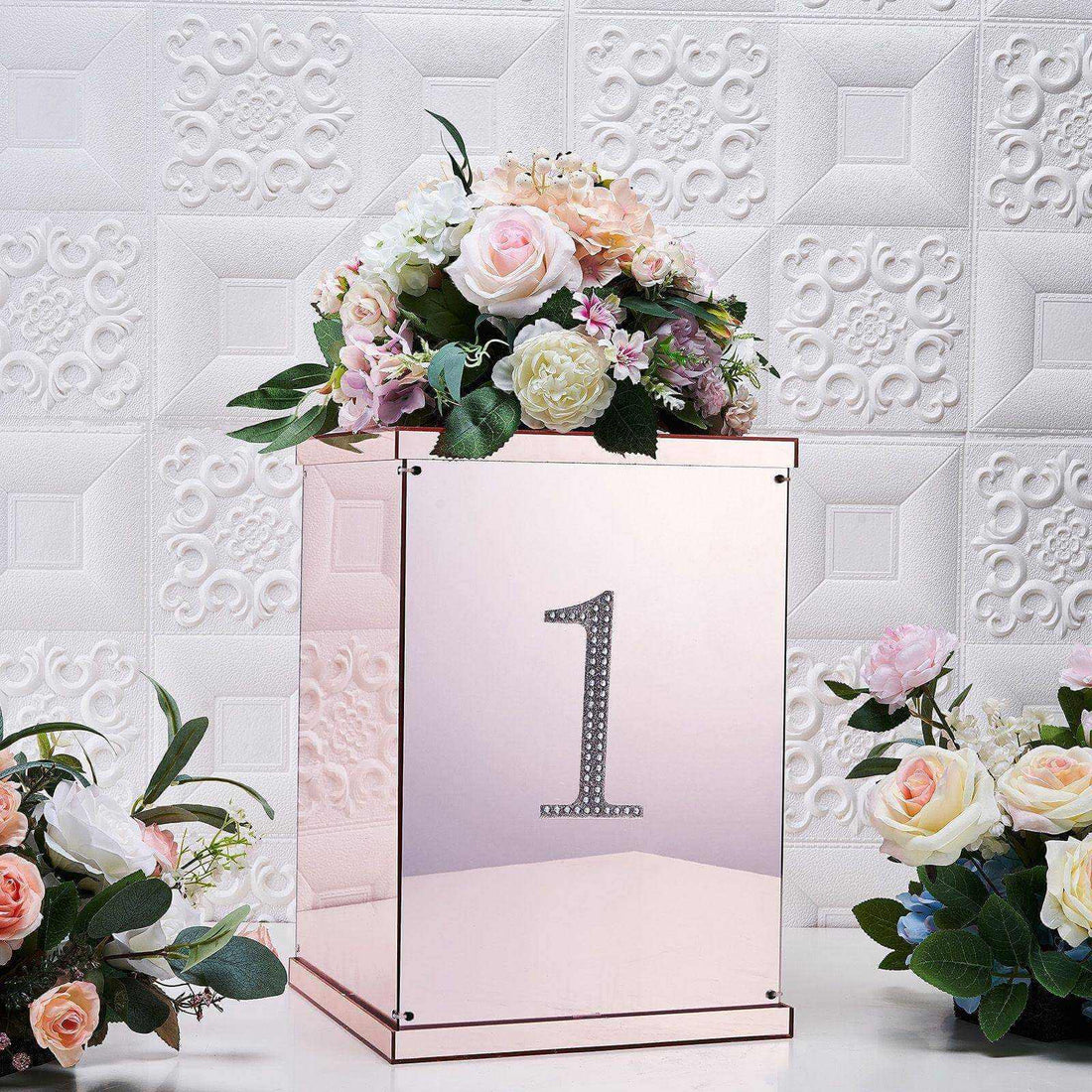Rose gold flower box with number one and floral arrangement on textured background.