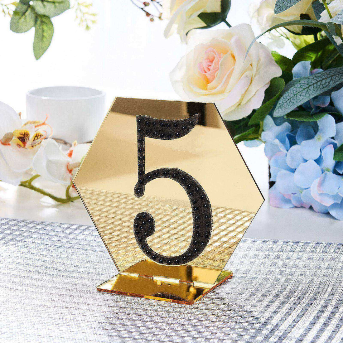 Gold hexagon table number 5 with black embellishments on a decorative table setting.