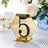 Gold hexagon table number 5 with black embellishments on a decorative table setting.