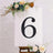 Decorative black number 6 on an easel with flowers around it.