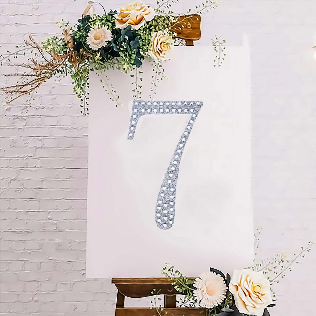 Decorative number 7 with rhinestones on an easel surrounded by flowers.