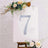 Decorative number 7 with rhinestones on an easel surrounded by flowers.