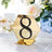 Gold hexagonal table number 8 with black embellishments on a reflective base.