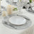 Elegant dining setup with a white plate, cutlery, and candles on a textured tablecloth.