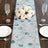 Floral table runner with green leaves on a rustic wooden table setting.