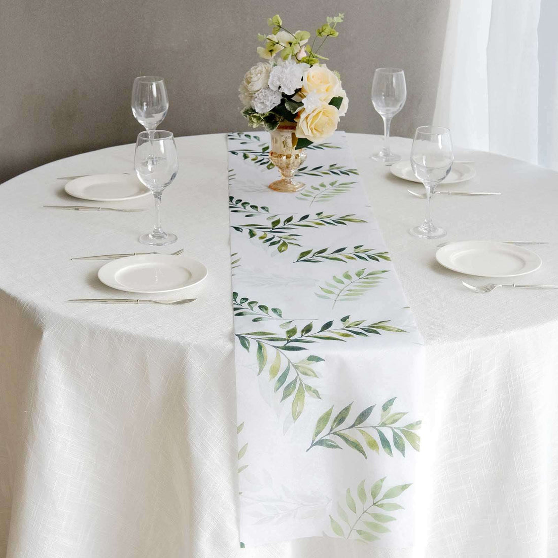 Floral table runner on a dining table with glasses and plates.