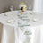 Floral table runner on a dining table with glasses and plates.