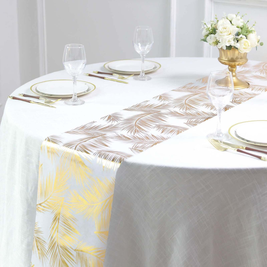 Elegant palm leaf table runner in gold and bronze on a dining table setting.