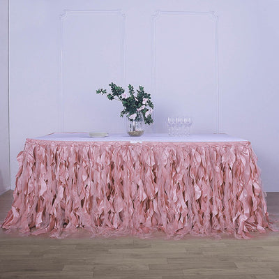 Pink ruffled table skirt with floral centerpiece and glassware on a table.