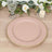 Pink decorative plate with gold trim on a wooden table with greenery and candles.