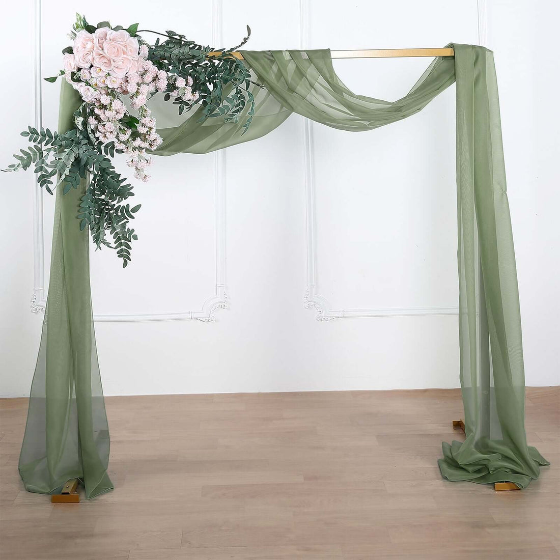 Wedding arch with greenery and pink flowers, draped in sheer fabric.