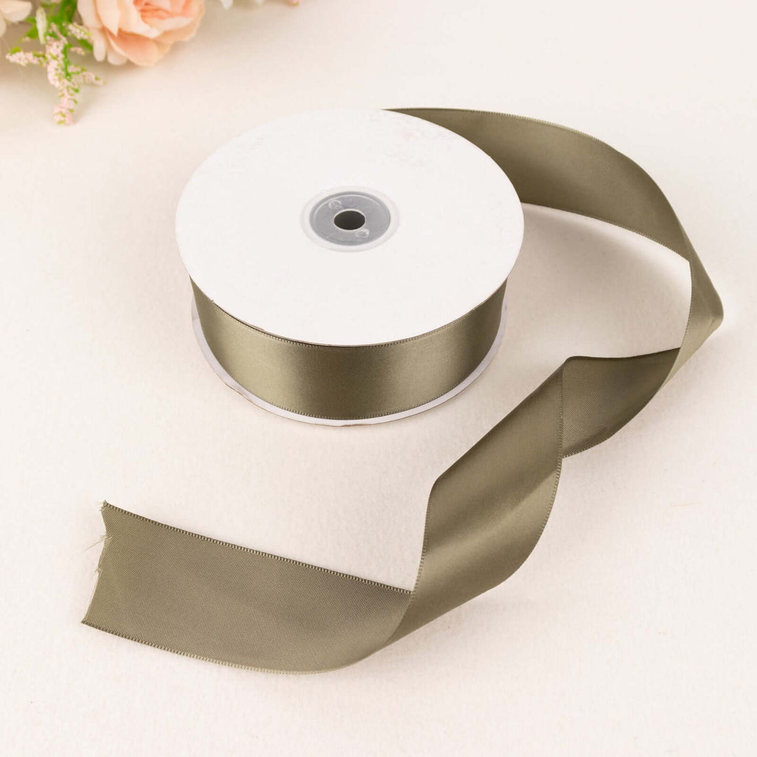 Olive green satin ribbon on a spool with a loose end