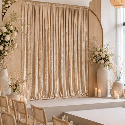 Elegant beige wedding stage with floral arrangements, candles, and draped curtain backdrop