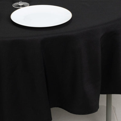 Black tablecloth draped over a table with a white plate and glass.