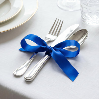 Elegant blue ribbon tied around silver cutlery on a white table setting