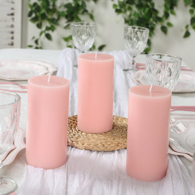 Three pink candles on a table with elegant glassware and a woven placemat.