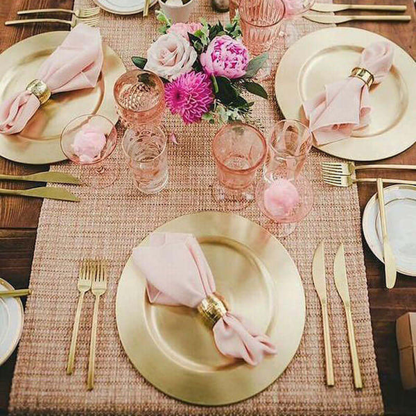 Elegant table setting with gold plates, pink napkins, and floral centerpiece.