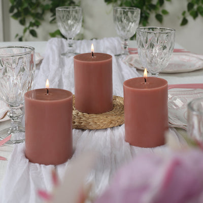 Three elegant candles on a table set with glassware and decorative accents.