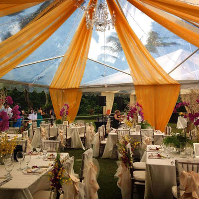 Elegant event tent with orange drapes and floral decorations, set for a celebration.